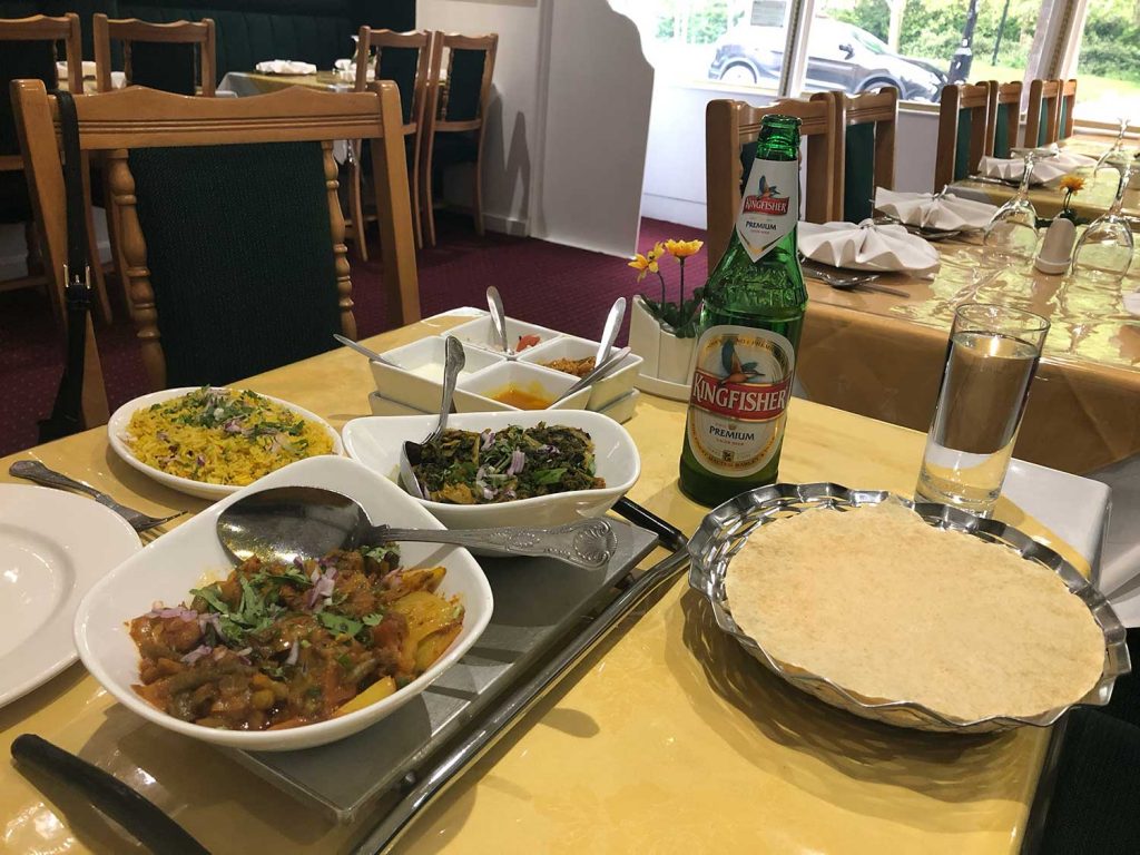 A table with curry, poppadoms and rice with a kingfisher beer