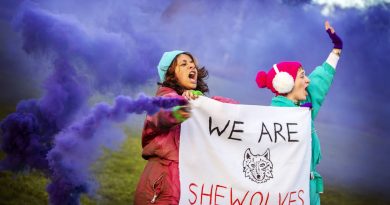 Actors holding banner and purple flares, from SHEWOLVES a Poplar Union play about teenage activism.