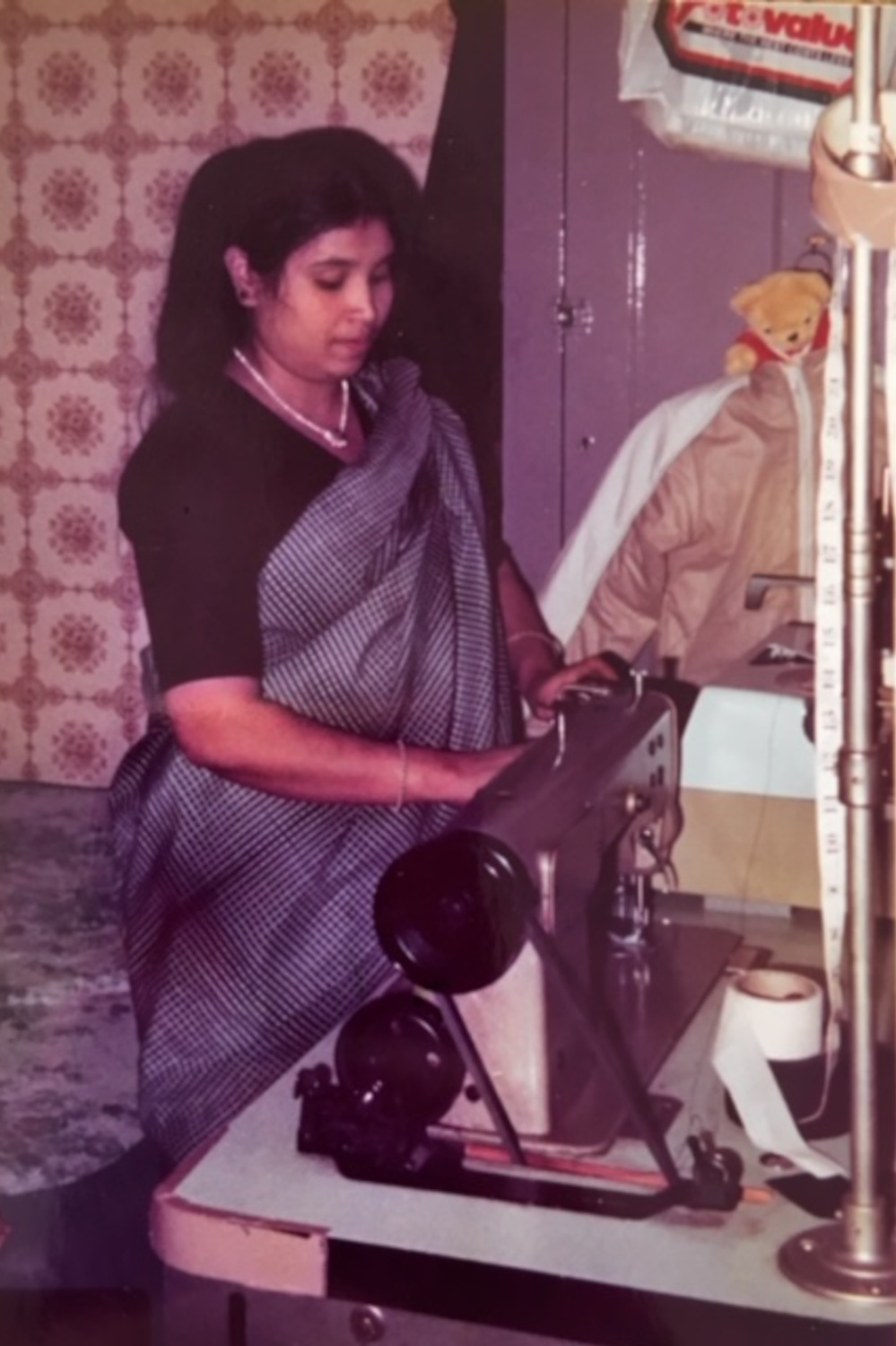 Bangladeshi seamstress Anwara Begum stands working at a sewing machine in her home in Shoreditch, East London