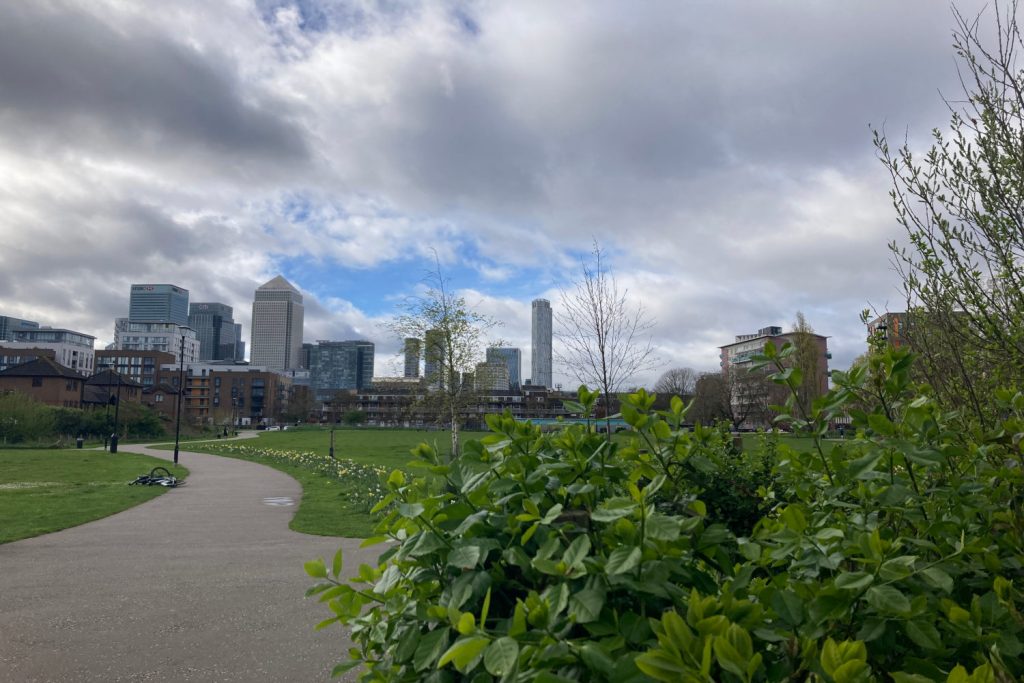 View of Bartlett Park with bushes in front of skyscrapers in Poplar, East London.