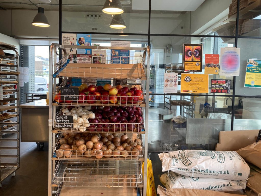 Shelves of apples and onions for sale next to bags of flour at e5 Poplar Bakehouse in East London.