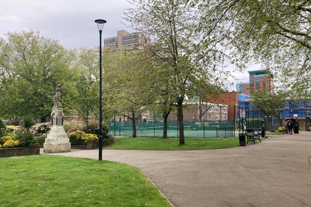 View of a statue and tennis court in the centre of Poplar Recreation Grounds, East London.