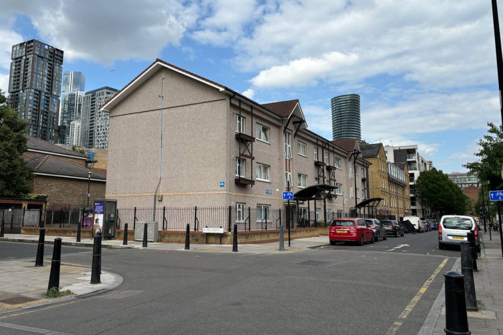 Low-rise apartment building on Tiller Road in East London, with modern skyscrapers in the background.
